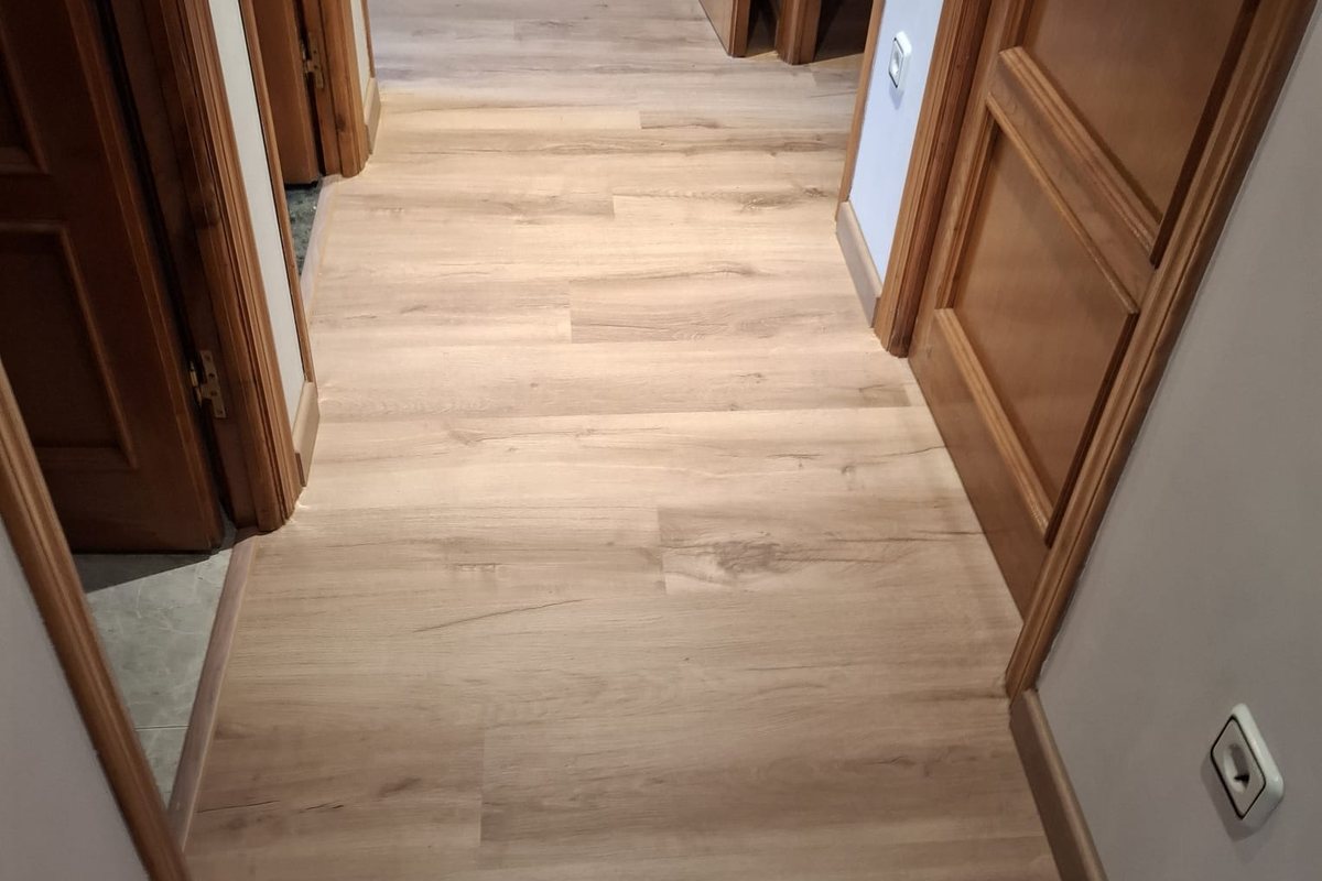 Pasillo con suelo laminado roble claro y rodapié, instalado bajo las puertas de madera